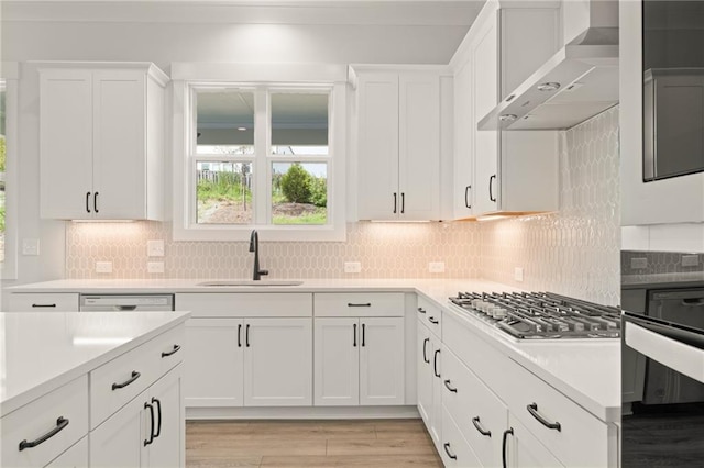 kitchen featuring stainless steel gas cooktop, backsplash, sink, wall chimney exhaust hood, and white cabinets