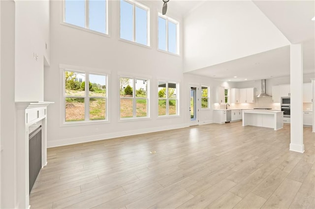 unfurnished living room with a healthy amount of sunlight, a towering ceiling, sink, and light hardwood / wood-style floors