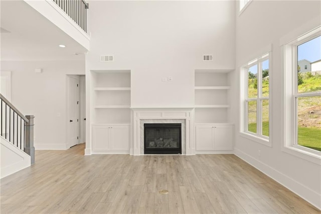 unfurnished living room featuring light wood-type flooring, built in shelves, a fireplace, and a towering ceiling