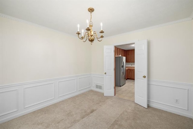 empty room with light colored carpet, a wainscoted wall, visible vents, an inviting chandelier, and crown molding