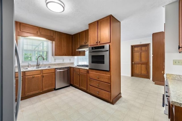 kitchen with stainless steel appliances, brown cabinetry, a sink, and light floors