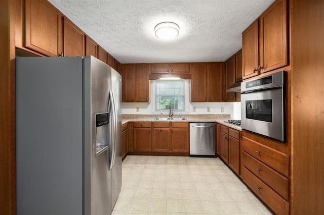 kitchen with a sink, light countertops, appliances with stainless steel finishes, light floors, and brown cabinetry