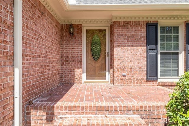 view of exterior entry featuring a shingled roof and brick siding