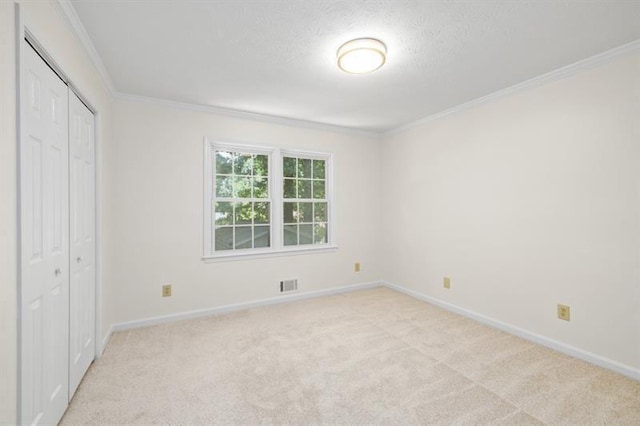 unfurnished bedroom with light colored carpet, visible vents, baseboards, a closet, and crown molding