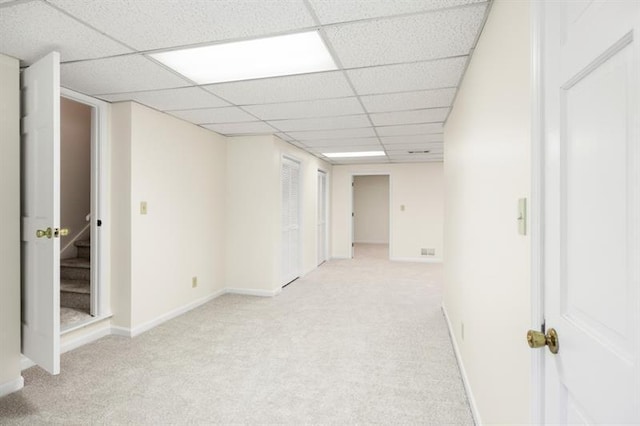 below grade area featuring a paneled ceiling, stairway, baseboards, and light colored carpet