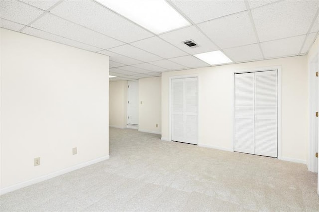 below grade area featuring baseboards, a paneled ceiling, visible vents, and light colored carpet