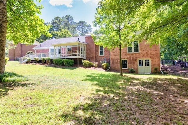 back of house with brick siding, a lawn, and a deck