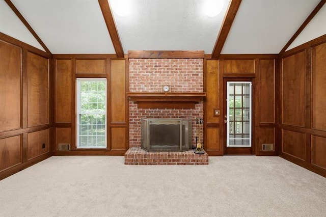 unfurnished living room with a brick fireplace, light colored carpet, vaulted ceiling with beams, and wood walls