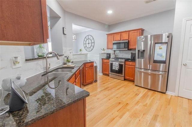 kitchen with light hardwood / wood-style flooring, appliances with stainless steel finishes, sink, and dark stone counters