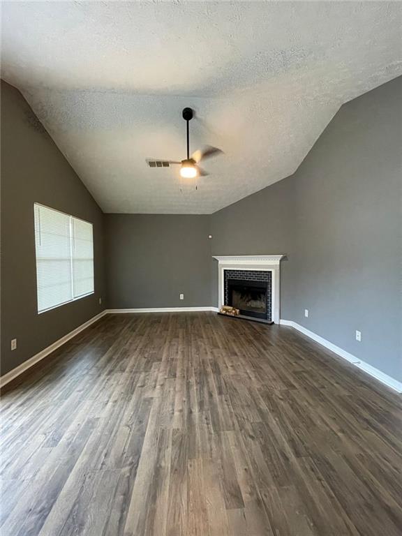 unfurnished living room featuring vaulted ceiling, dark wood finished floors, and a fireplace