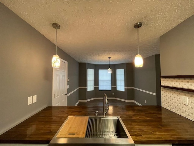 kitchen with baseboards, wood counters, wood finished floors, a textured ceiling, and pendant lighting