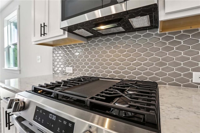 kitchen featuring decorative backsplash, appliances with stainless steel finishes, white cabinetry, and light stone countertops