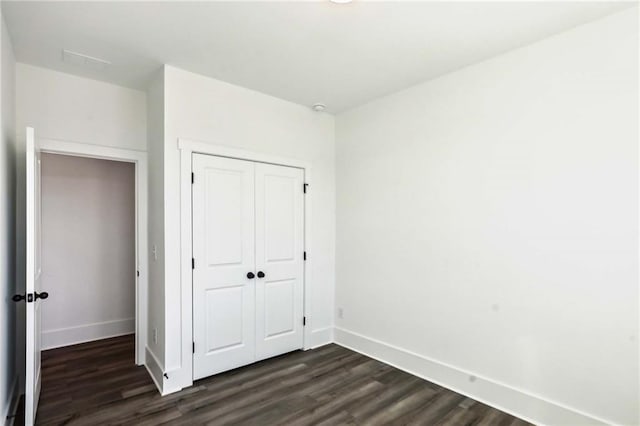 unfurnished bedroom featuring a closet, baseboards, and dark wood-type flooring