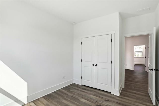 unfurnished bedroom featuring a closet, baseboards, visible vents, and dark wood-style flooring