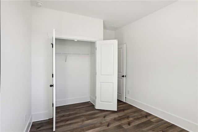 unfurnished bedroom with a closet, baseboards, and dark wood-style floors