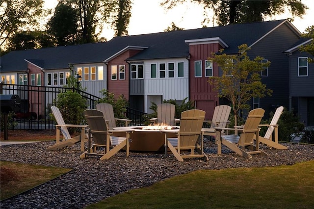 back of house at dusk featuring board and batten siding, an outdoor fire pit, a patio, and fence