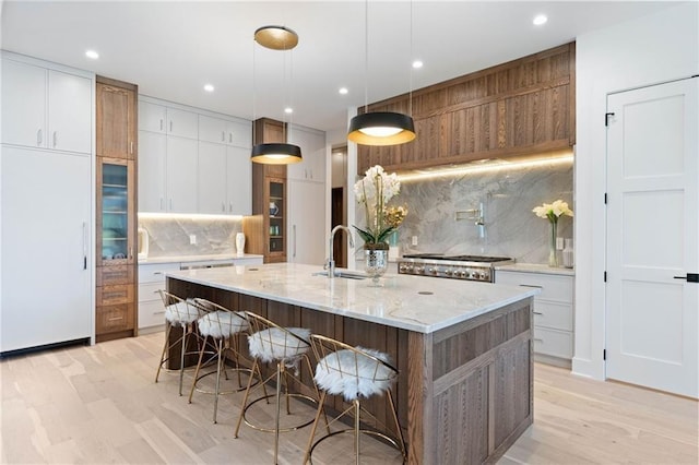 kitchen with decorative backsplash, white cabinets, sink, pendant lighting, and a center island with sink