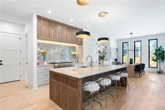 kitchen with white cabinets, light hardwood / wood-style flooring, hanging light fixtures, and sink