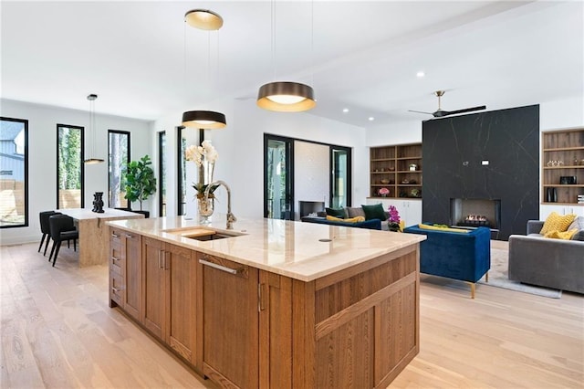 kitchen with light hardwood / wood-style flooring, a center island with sink, sink, a fireplace, and hanging light fixtures