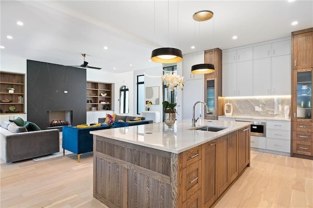 kitchen with a center island with sink, light wood-type flooring, sink, and white cabinets