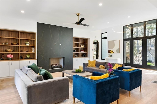 living room featuring light wood-type flooring, a high end fireplace, and ceiling fan