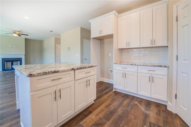 kitchen with light stone countertops, ceiling fan, dark hardwood / wood-style floors, decorative backsplash, and white cabinets