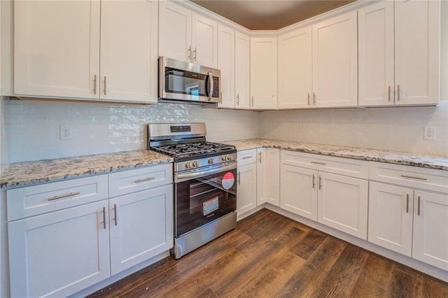 kitchen with light stone countertops, stainless steel appliances, white cabinetry, and dark wood-type flooring