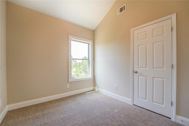 spare room featuring light colored carpet and vaulted ceiling