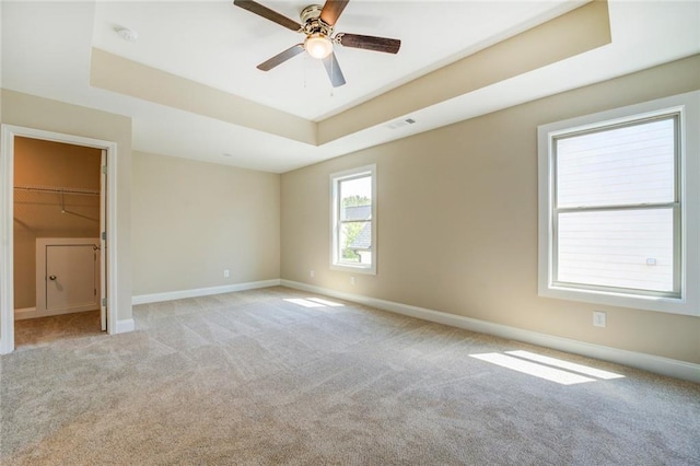 unfurnished bedroom with ceiling fan, light colored carpet, a walk in closet, and a tray ceiling