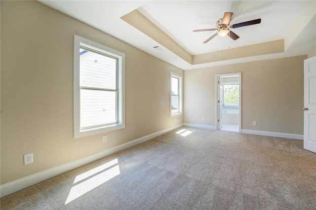 unfurnished room featuring light carpet, a tray ceiling, and ceiling fan