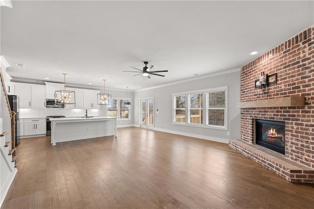 kitchen featuring a fireplace, a sink, stainless steel appliances, ceiling fan with notable chandelier, and open floor plan