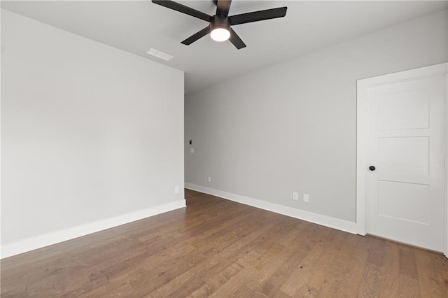 empty room with wood finished floors, a ceiling fan, baseboards, and visible vents