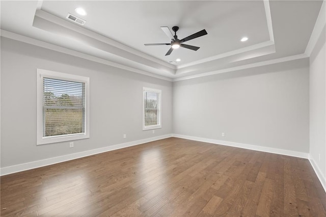 empty room featuring a ceiling fan, baseboards, visible vents, a tray ceiling, and dark wood-type flooring