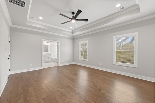 unfurnished bedroom featuring a tray ceiling, multiple windows, and visible vents