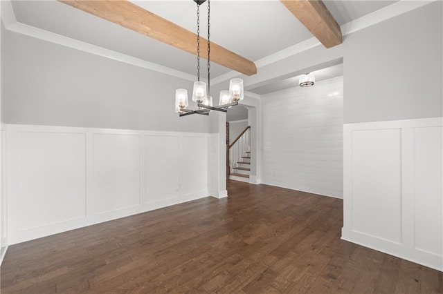 unfurnished dining area with beam ceiling, a notable chandelier, dark wood finished floors, stairway, and wainscoting