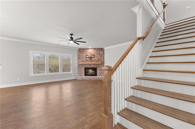 unfurnished living room with crown molding, stairs, a fireplace, wood finished floors, and a ceiling fan