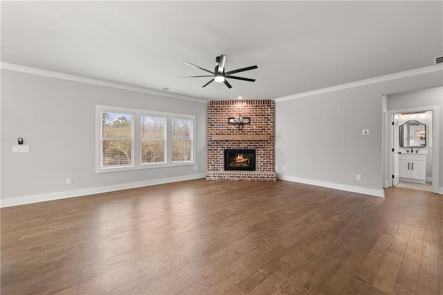 unfurnished living room with ornamental molding, a ceiling fan, dark wood finished floors, a fireplace, and baseboards