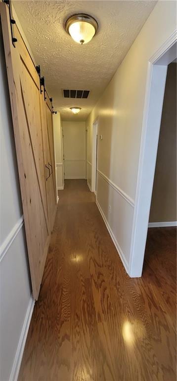 hallway with a textured ceiling, a barn door, visible vents, and wood finished floors