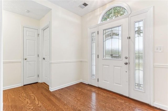 entrance foyer with a textured ceiling, baseboards, visible vents, and wood finished floors