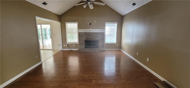 unfurnished living room with ceiling fan, a brick fireplace, visible vents, and wood finished floors