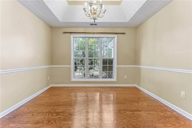unfurnished room with a notable chandelier, a textured ceiling, baseboards, visible vents, and wood finished floors