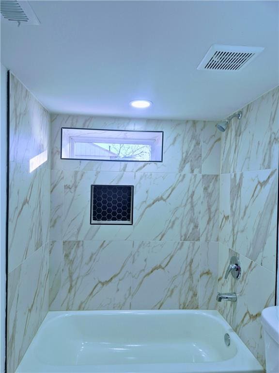 bathroom featuring toilet and tiled shower / bath