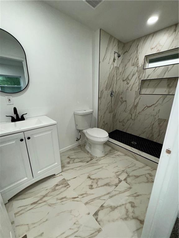 bathroom with tiled shower, vanity, and toilet