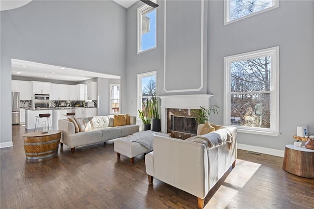 living room featuring dark hardwood / wood-style flooring, a towering ceiling, and a premium fireplace