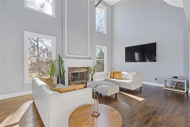 living room featuring a premium fireplace, dark wood-type flooring, and a towering ceiling