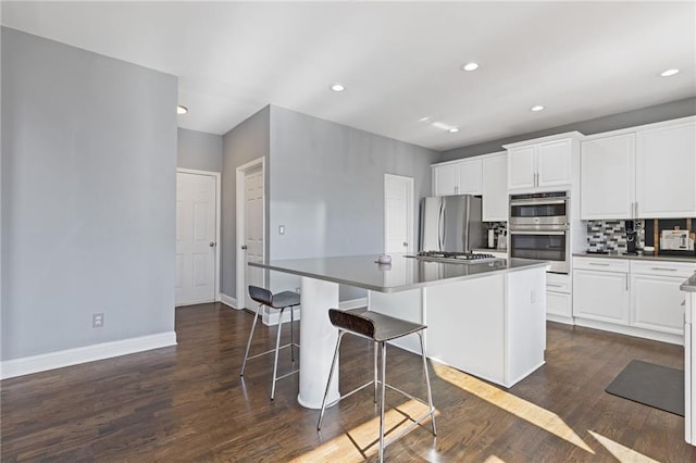 kitchen featuring white cabinetry, a kitchen bar, decorative backsplash, stainless steel appliances, and a center island with sink