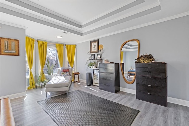 living area with a tray ceiling, ornamental molding, and light wood-type flooring