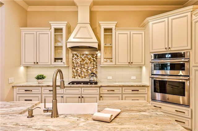 kitchen with tasteful backsplash, light stone counters, custom range hood, and appliances with stainless steel finishes