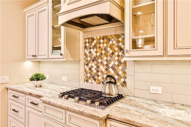 kitchen featuring stainless steel gas stovetop, light stone countertops, custom range hood, and backsplash