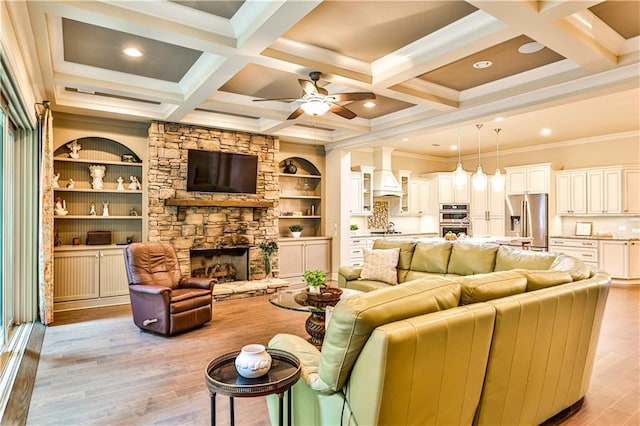 living room featuring ceiling fan, coffered ceiling, a stone fireplace, beamed ceiling, and light wood-type flooring